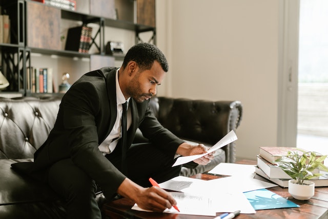 person in black suit reviewing several documents spread out on a table